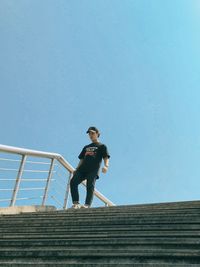 Low angle view of man on staircase against clear blue sky