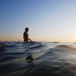 Man in sea against clear sky during sunset