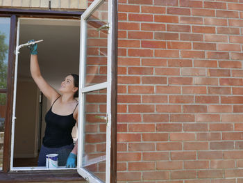 Smiling young woman painting window frame