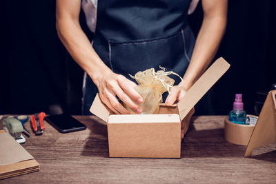 Midsection of woman packing gift in box on table