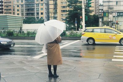 Rear view of man with umbrella on street in rainy season