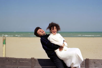 Portrait of smiling woman standing at beach against clear sky