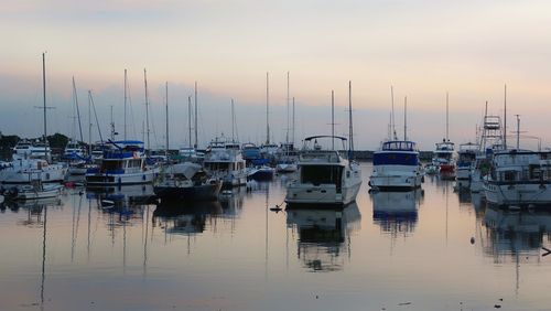 Sailboats moored in sea against sky during sunset