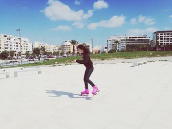 Side view of girl roller skating on field against cloudy sky