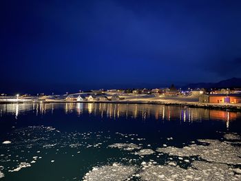 Illuminated buildings by sea against blue sky at night