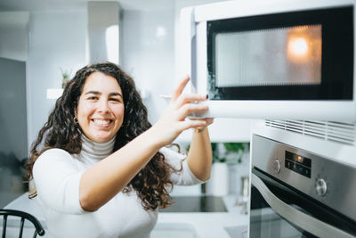 Portrait of young woman opening microwave open