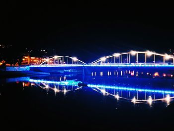 Light trails on river against blue sky at night