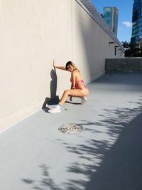 Full length of woman crouching by wall in bikini outdoors