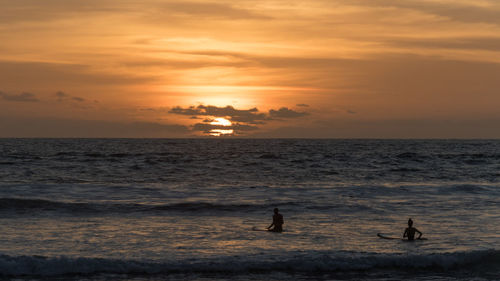 Silhouette people on beach against sky during sunset