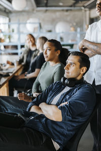 Computer programmer with arms crossed wearing headphones sitting with colleagues in office