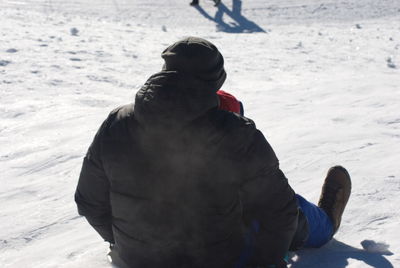 Rear view of man sitting on snow covered land