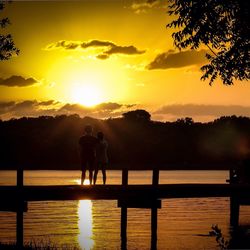 Silhouette friends standing on jetty against sea during sunset