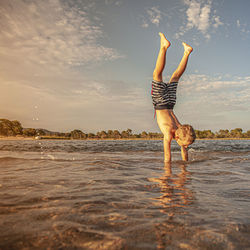 Boy doing handstand at beach against sky