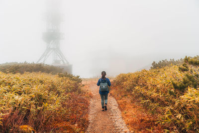 Rear view of woman walking on dirt road against sky