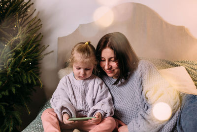 Mom and daughter look at the smartphone at christmas together