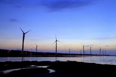 Silhouette wind turbines on land against sky during sunset