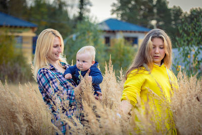A young mother walks with her children in a field with tall grass.
