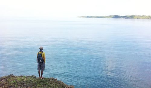 Rear view of man standing on rock against sea
