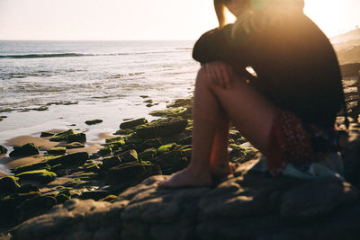 Midsection of woman sitting on beach against sea