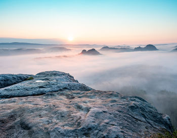Mountain top rock, sleepy misty landscape bellow under heavy morning fog