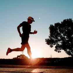 Low angle view of man running on footpath against clear sky during sunset