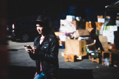 Young woman using mobile phone while standing on street at night