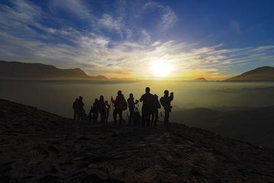 People standing on desert against sky during sunset