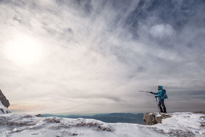 Side view of man showing with hiking pole while standing on snow against sky