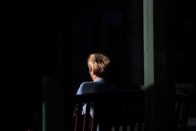 Rear view of woman sitting on bench in darkroom