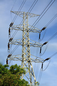 Low angle view of electricity pylon and trees against blue sky