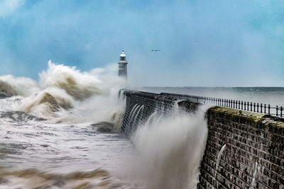 Waves crashing on pier against sky