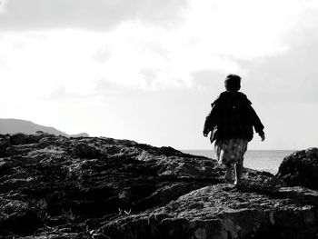 Rear view of man standing on rock against sky