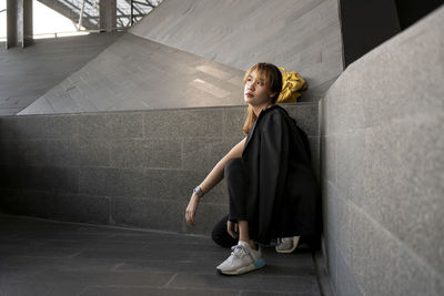 Thoughtful businesswoman crouching on floor by wall