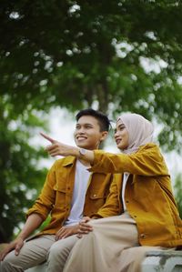 Young couple looking away while sitting against blurred background