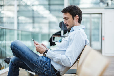 Businessman waiting in airport departure area, using digital tablet