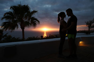 Couple embracing while standing against sky during sunset