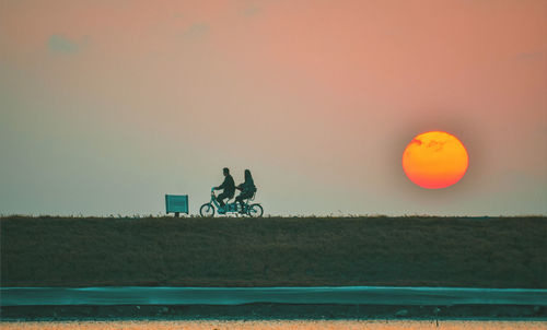 Men riding bicycle on field against sky during sunset