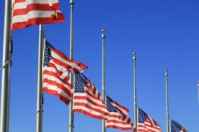 Low angle view of american flags against clear blue sky