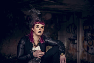 Portrait of young woman smoking cigarette while sitting in abandoned building