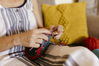 Mature woman knitting while sitting on sofa at home