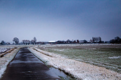 Snow covered road by field against clear sky