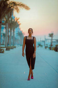 Full length portrait of young woman standing against trees