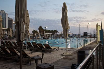 Chairs by swimming pool in city against sky