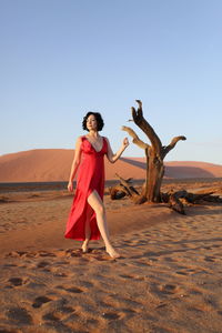 Portrait of young woman standing on sand dune in desert against clear sky