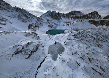 Three mountain frozen turquoise lakes in the snowy mountains, top view from a drone