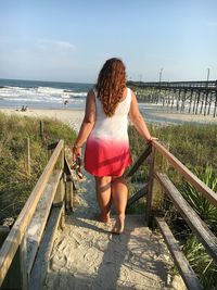 Rear view of woman standing on beach against sky