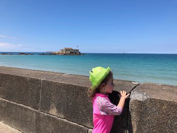 Girl standing by retaining wall against sky