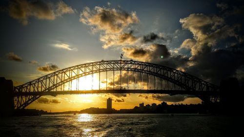 Silhouette bridge over river against sky during sunset