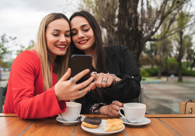 Smiling young woman using smart phone on table