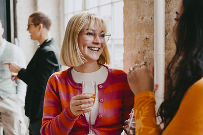 Happy blond businesswoman enjoying drink with female colleague during event at convention center